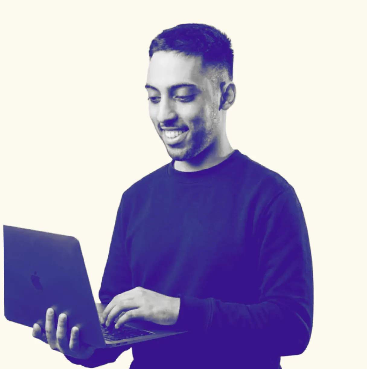 Smiling man holding and typing on an open laptop with a light background.